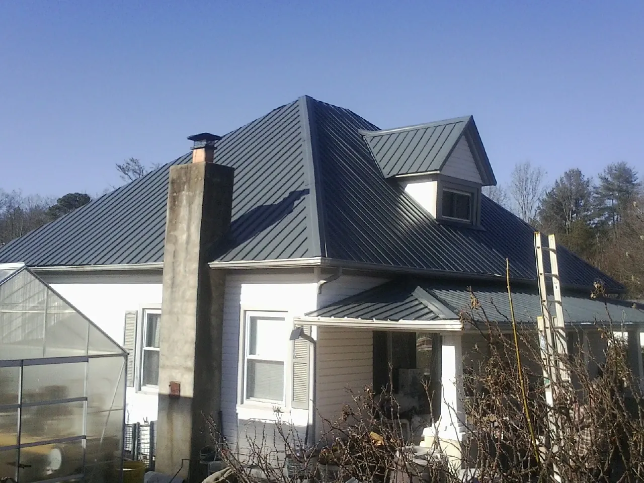 Dark blue standing seam metal roof on a white farmhouse with dormer — Slate & Tile Roof Repair by Roofing Brothers in Glenns Ferry