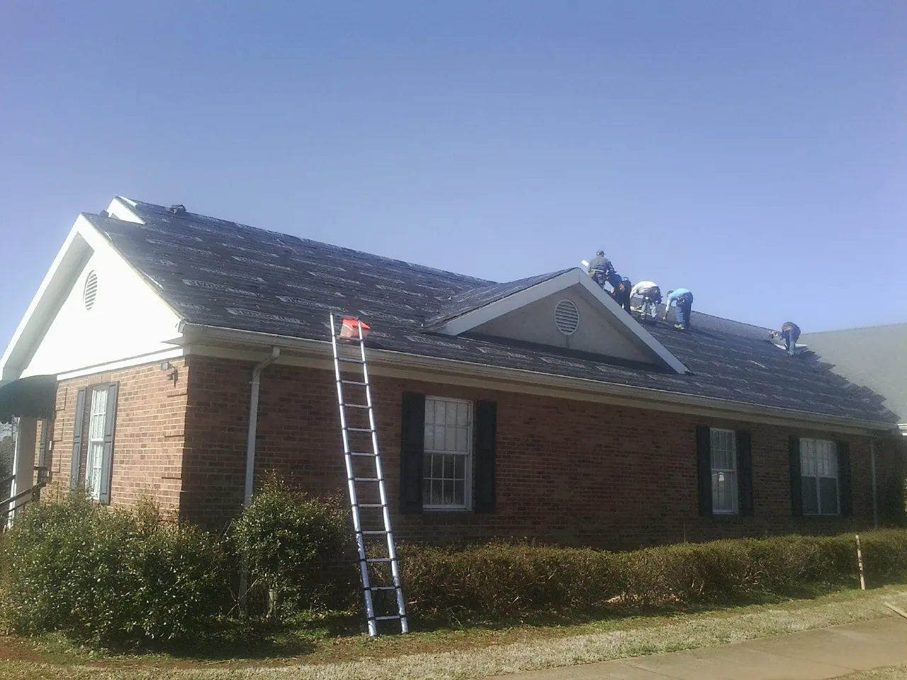 Crew tearing shingles off a brick ranch roof with a ladder set — Emergency Roof Repair work by our crew in Glenns Ferry