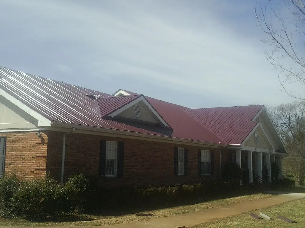 Red metal roof with gabled entries on a long brick building, from a Hail Damage Roof Repair job in Glenns Ferry