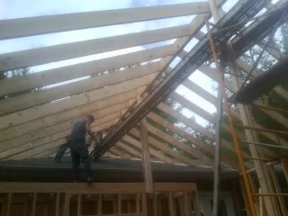 Rafters going up over a new addition with a worker on the wall in Glenns Ferry