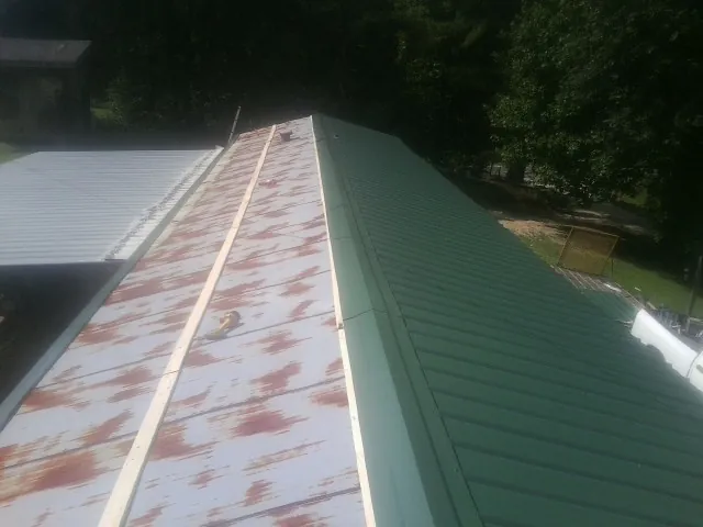 Old rusted panels beside newly installed green metal roofing — Wind Damage Roof Repair by Roofing Brothers in Glenns Ferry