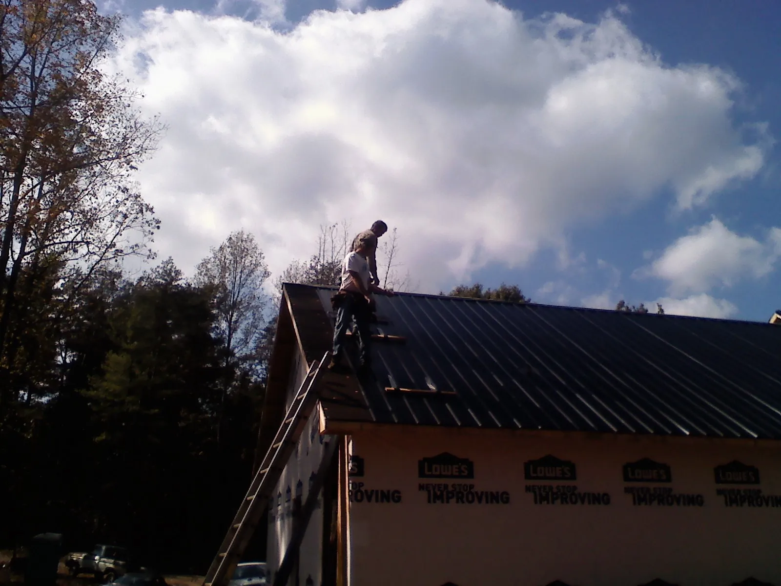 Roofer fastening dark metal panels high against a cloudy sky, from a Roof Inspection job in Glenns Ferry