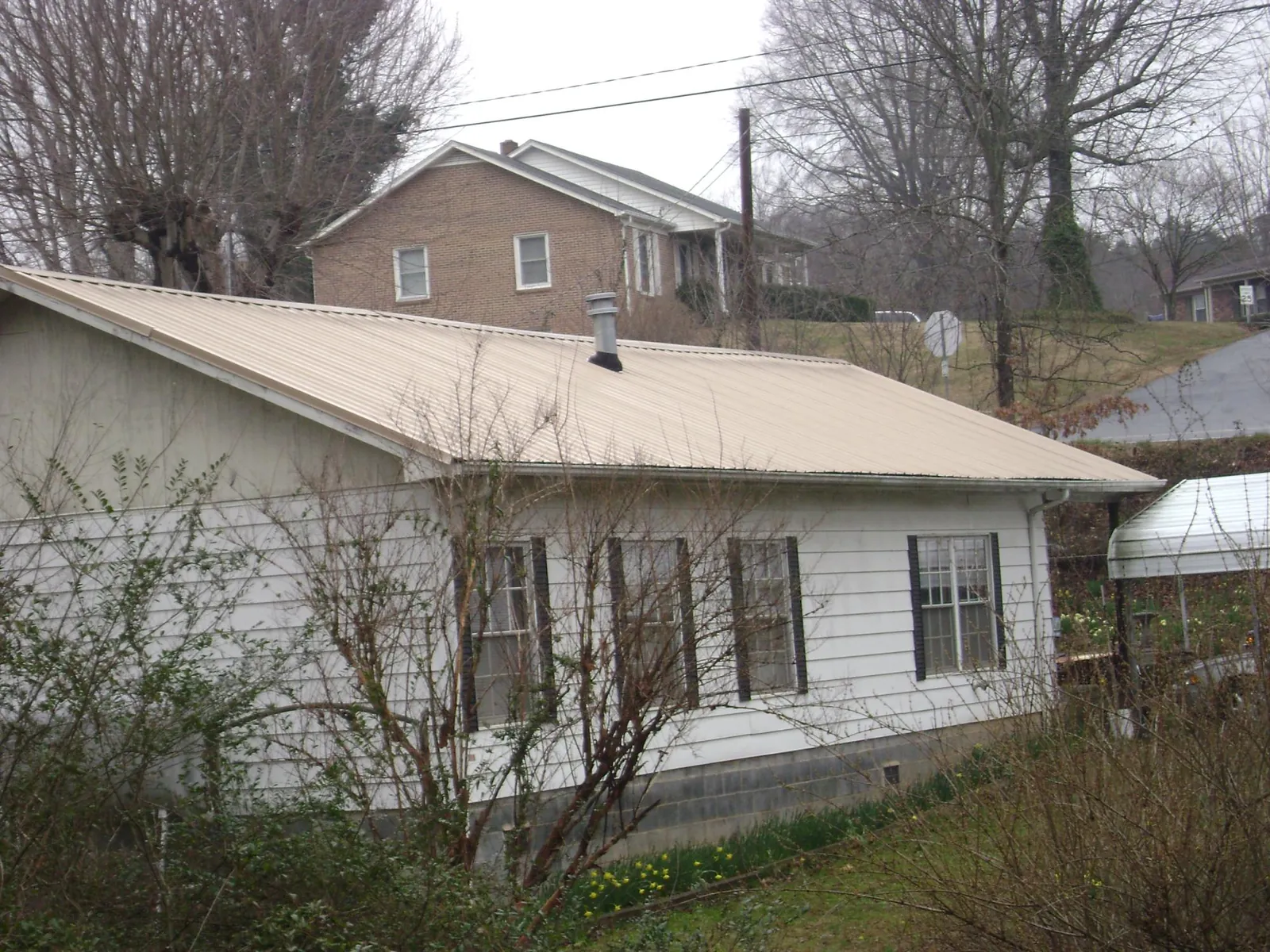 Tan metal roof on a white sided house set into a hillside — Commercial Roofing by Roofing Brothers in Glenns Ferry